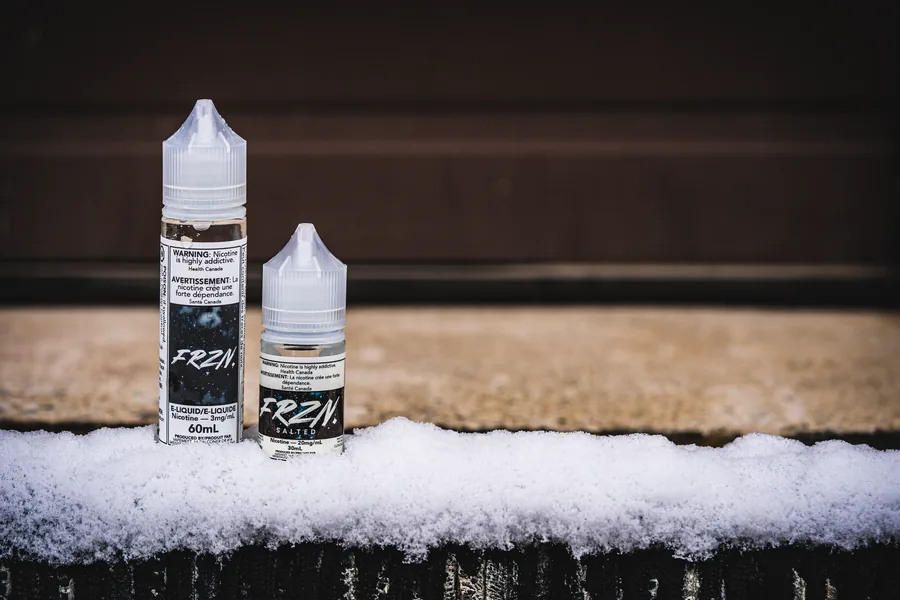 Two FRZN e-liquid bottles, 60mL and 30mL, standing on a snowy ledge