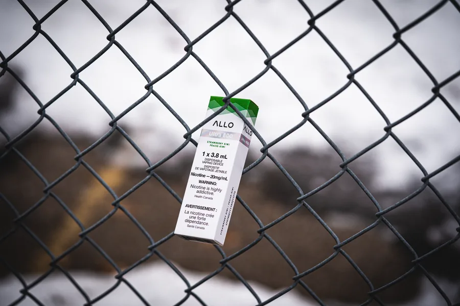 An Allo Ultra 800 strawberry kiwi box tucked into a chain link fence with snow behind