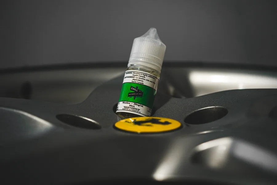 A green labelled Chill St 30mL bottle sitting on a silver car wheel with a yellow centre cap