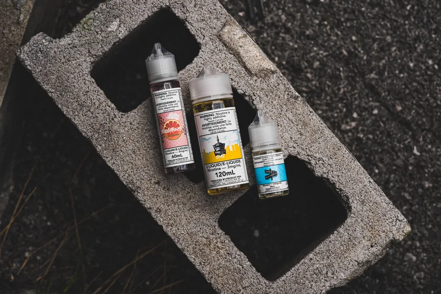 Three e-liquid bottles of different sizes lying on a grey cinder block seen from above