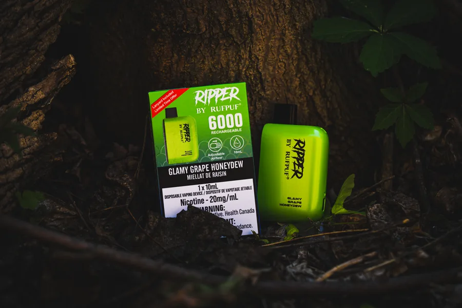 A lime green Ripper disposable and its box at the base of a tree among leaves