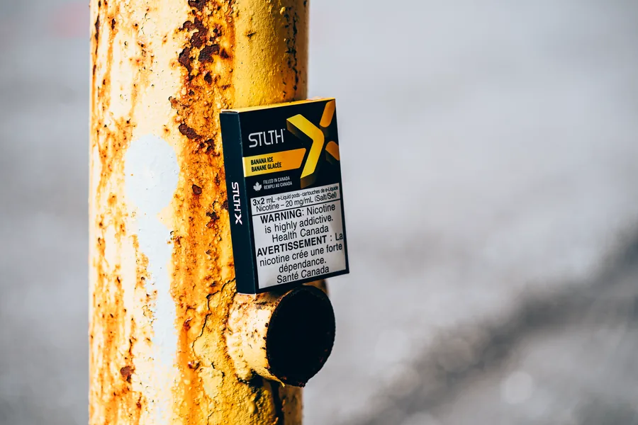 A black and gold STLTH X Banana Ice pod pack attached to a rusted yellow pole