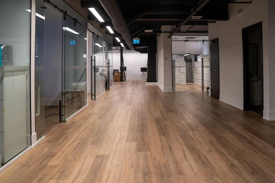 Long corridor with wood look flooring and glass office walls on the left