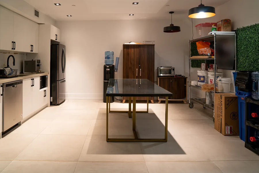 Staff kitchen with white cabinets, stainless appliances and a black stone table under a pendant light