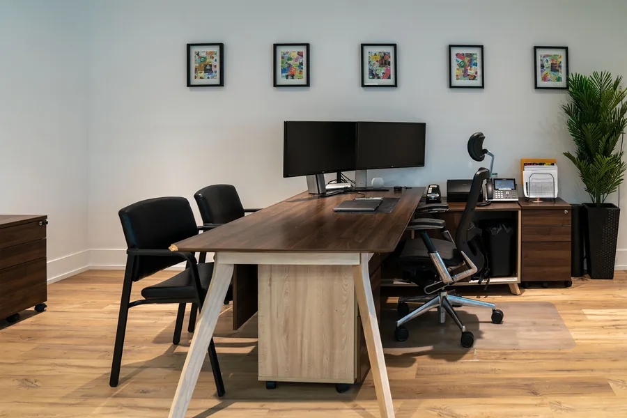 Private office with a wood desk, black chairs, framed prints and a potted plant