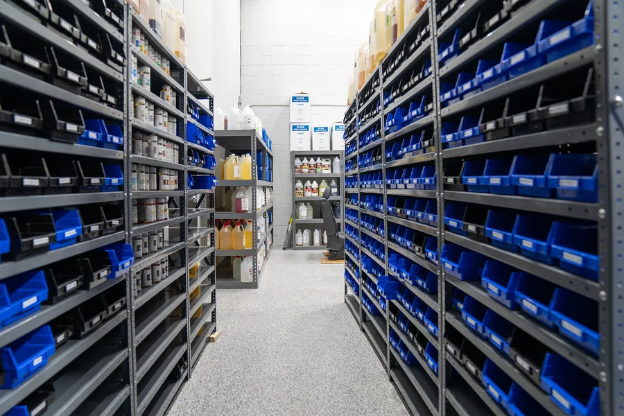 Warehouse aisle lined with grey shelving full of blue and black bins
