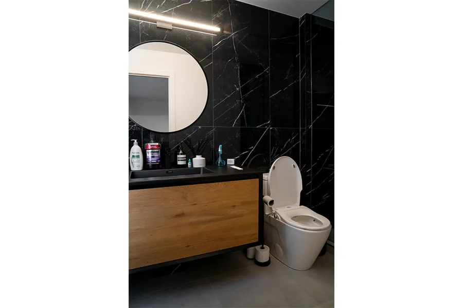 Modern powder room with black tile, a round mirror and a floating wood vanity