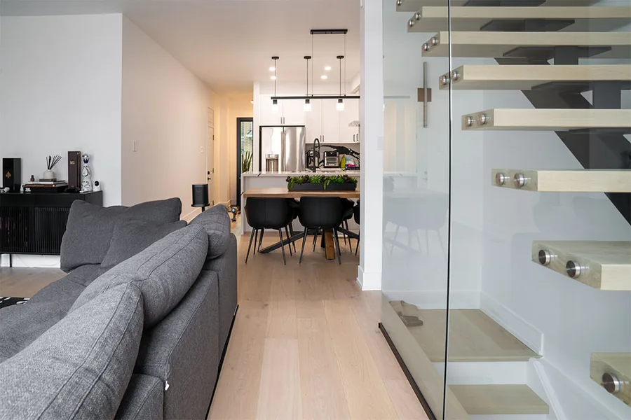 Bright living room with a grey sofa next to a floating staircase with glass railings