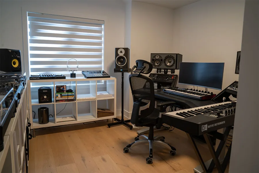 Home studio with a desk, monitors, speakers and a keyboard under a window