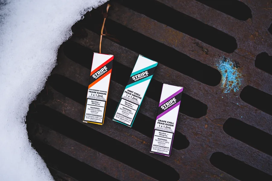 Three Stripe boxes in orange, teal and purple leaning on a rusty storm grate with snow around it
