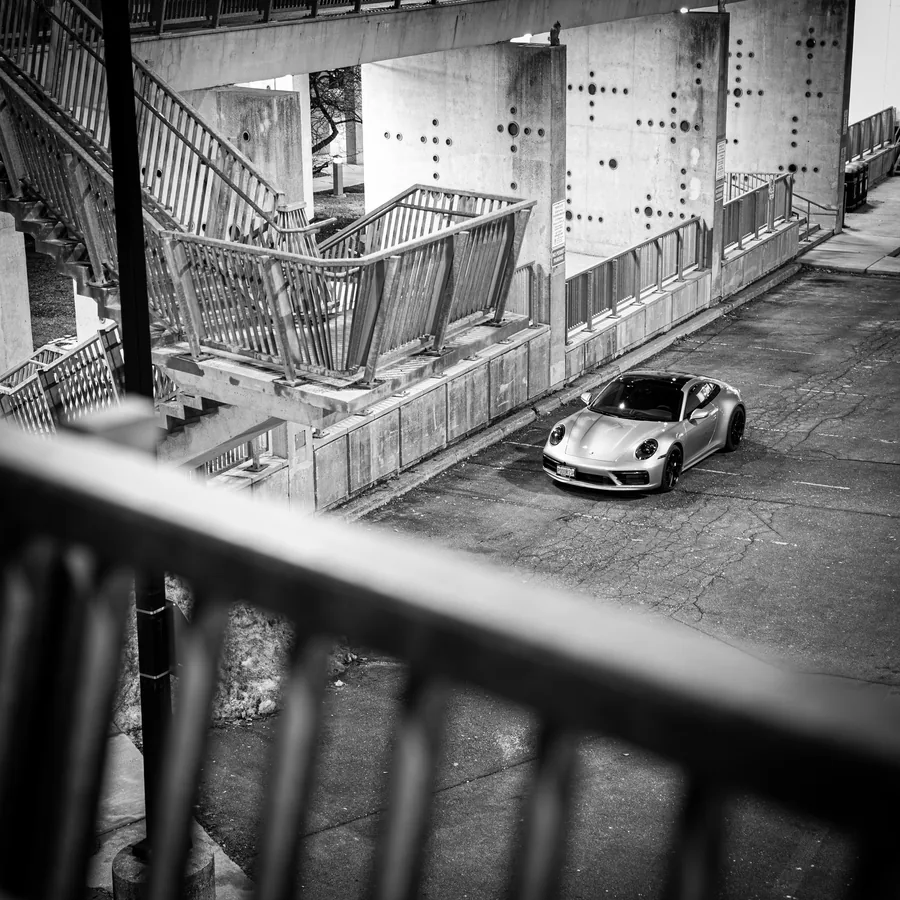 Black and white photo looking down a concrete stairwell at a Porsche 911 parked below