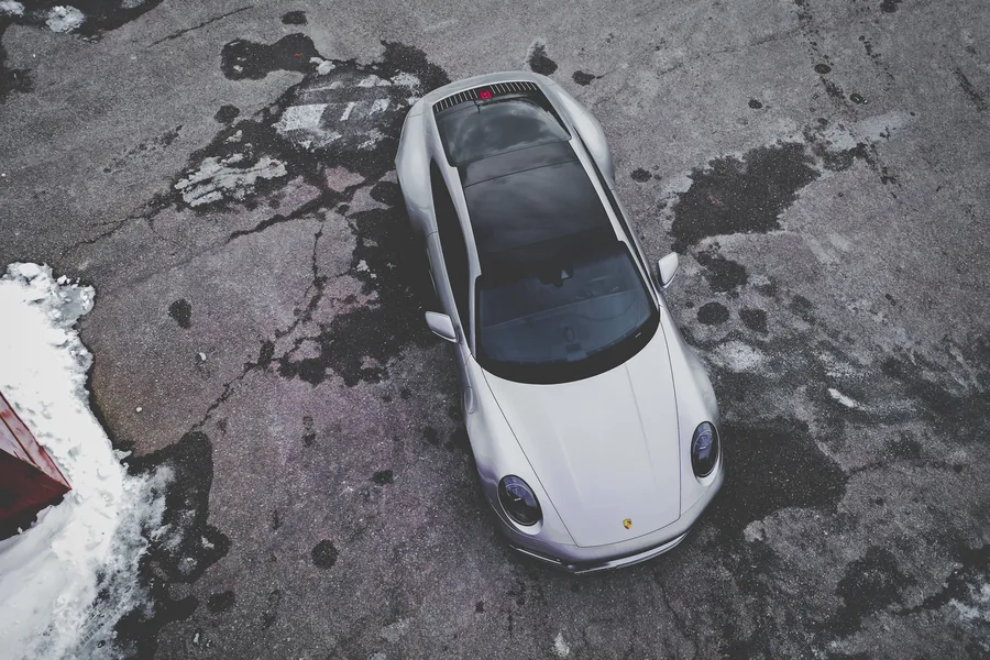 A silver Porsche 911 seen from directly above on cracked pavement with patches of snow