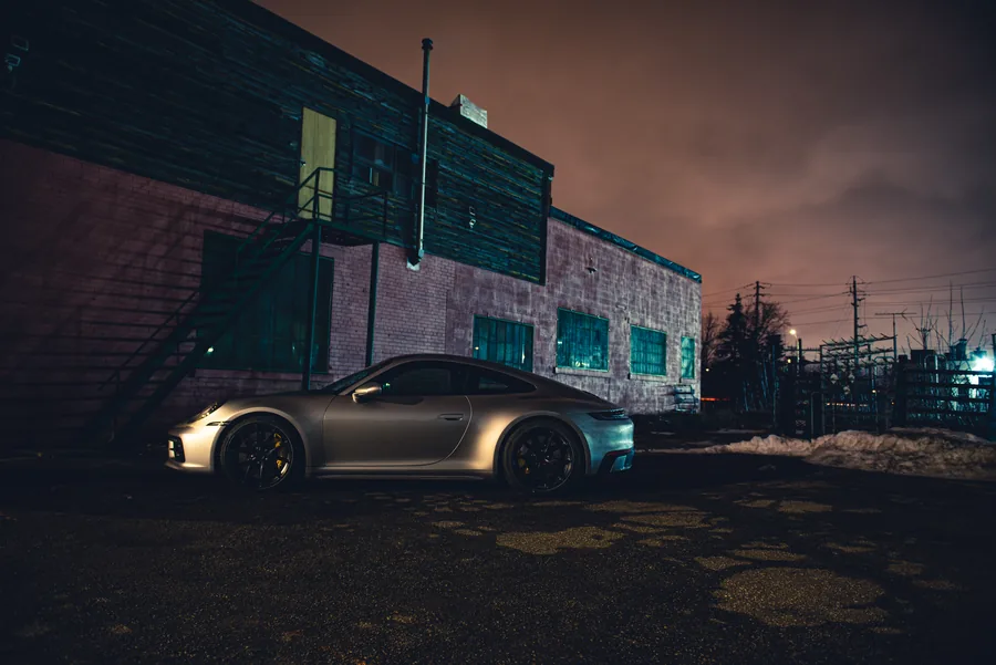 A silver Porsche 911 parked by an old brick building at night under an orange sky