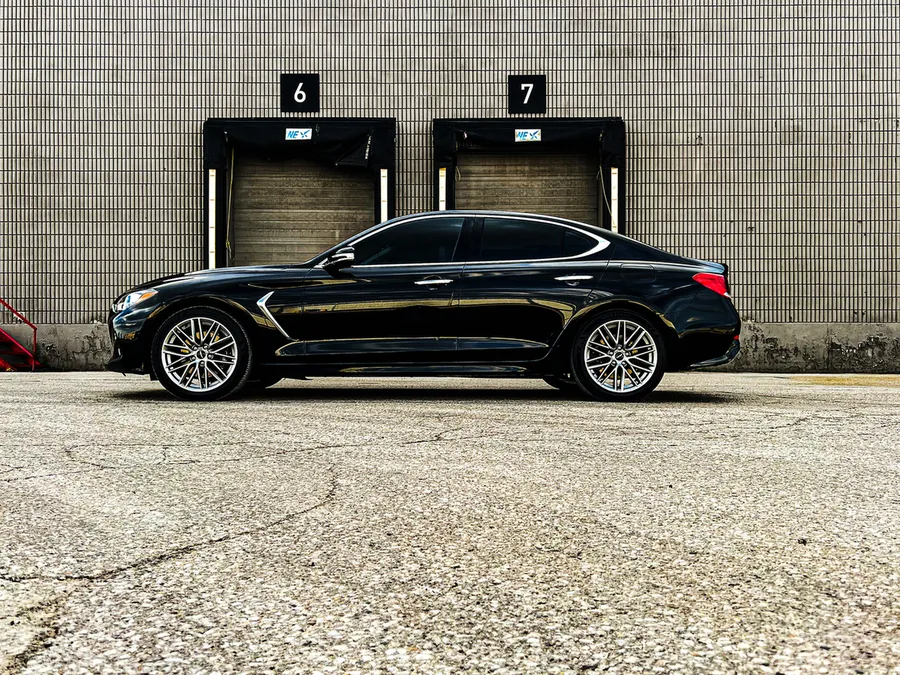 A black Genesis sedan parked in front of a row of loading dock doors